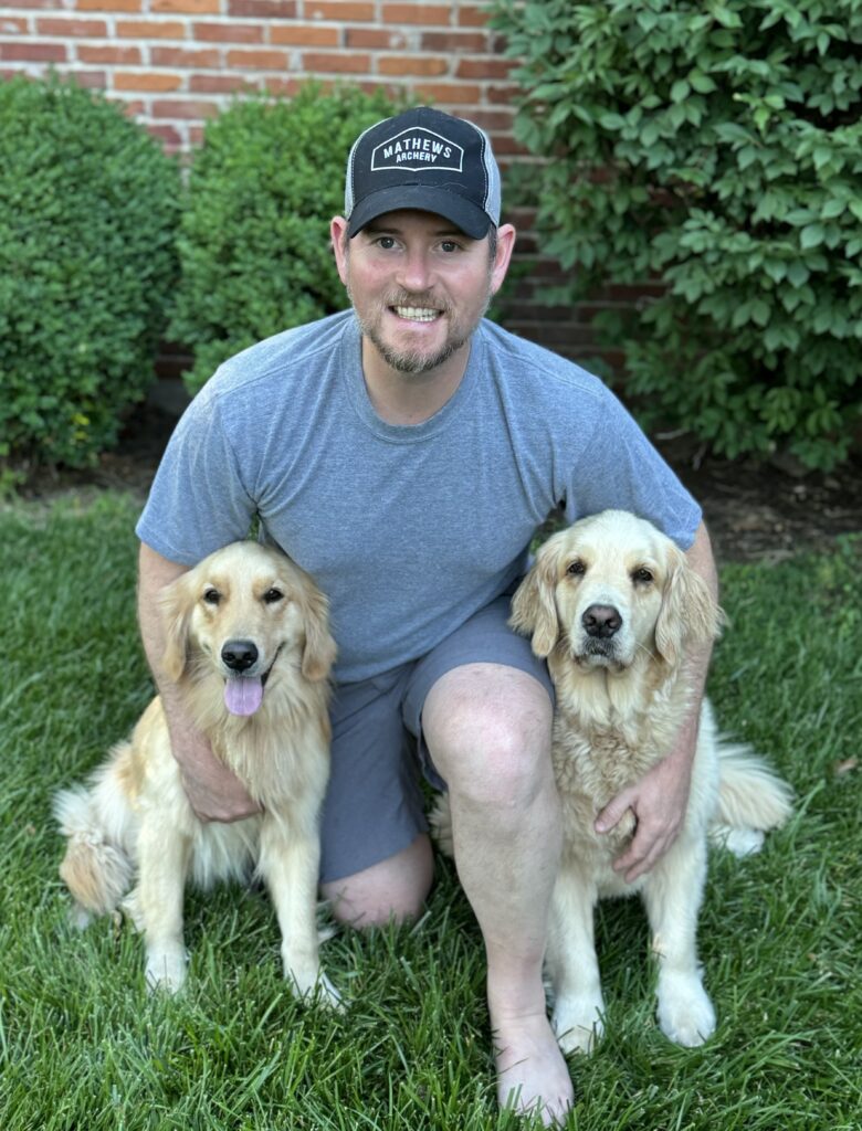 A man kneeling down with two dogs in his lap.