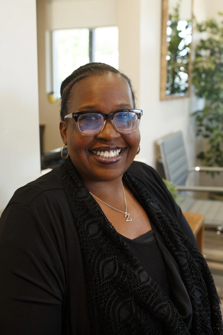 A woman with glasses and black jacket smiling.