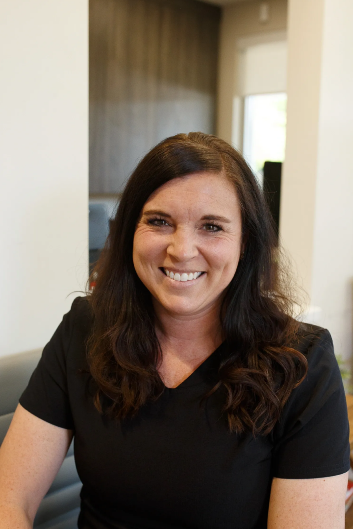 A woman smiling for the camera in front of a wall.