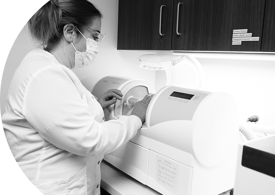 A woman in white lab coat and mask working on something.